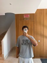 Remera gris con efecto acid wash y diseño oversize. Presenta un estampado frontal con la inscripción "KILLING IN THE NAME OF" y la frase "NOW YOU DO WHAT THEY TOLD YA".