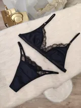 Conjunto de lencería compuesto por un corpiño triangular y una bombacha, ambos confeccionados en algodón negro con detalles de encaje en los bordes. El corpiño cuenta con breteles regulables y la bombacha presenta un diseño con tiras laterales.