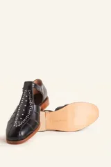 Sandalias de cuero color marrón, tipo romanas, con talón cerrado, tira en T con detalles de tachas metálicas, aberturas laterales y cierre de hebilla ajustable. Tienen tacón bajo de madera.