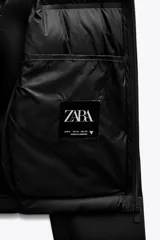 Chaqueta acolchada negra con cuello subido y capucha ajustable con cordones elásticos y stopper. Mangas largas combinadas en tejido efecto neopreno. Bolsillos laterales y cierre frontal con cremallera termosellada.