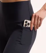 Pantalón corsario deportivo negro, confeccionado en poliamida y elastano, con cintura alta, bolsillos laterales y detalle de línea contrastante en el lateral.
