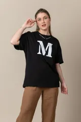 Remera gris con estampa de la letra M en negro y cadena plateada en el cuello.