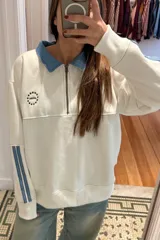Buzo de algodón color bordó con cuello camisero y medio cierre frontal de denim celeste. Presenta tiras laterales en las mangas en el mismo tono de denim y un logotipo bordado en el pecho con diseño circular de estrellas y la inscripción ANTHEA.