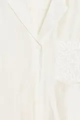 Camisa de manga larga color marrón oscuro, con cuello solapa, escote pico y bajo asimétrico. Presenta un bolsillo plastrón en el delantero con bordado combinado a tono.