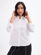 Camisa blanca de manga larga, con cuello clásico y cierre frontal de botones.