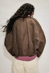 Chaqueta de efecto ante color marrón claro, con cuello solapa, manga larga con trabillas en los hombros y bajo abullonado. Cierre frontal con cremallera y botones ocultos por solapa.