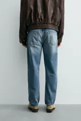 Pantalón de jean con corte recto desde la cadera hasta el tobillo, de tiro medio y ajuste holgado. Presenta diseño de cinco bolsillos, cierre frontal con cremallera y botón, y acabado con efecto lavado.