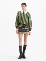 Minifalda de cuero ovino color marrón oscuro con bordados florales en tonos amarillos y verdes. Presenta un ruedo con detalle de piel sintética afelpada y una estructura definida.