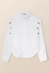 Camisa blanca de corte ancho con botones a presión ocultos y sisas decoradas con botones a presión dorados con forma de sol.