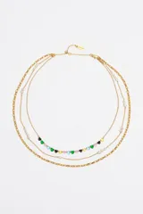 Collar de triple capa en tono dorado con cierre de mosquetón y largo regulable. Presenta una cadena interior con dijes de corazones en cristales de diversos colores (verde, rosado, celeste, amarillo y negro) y dos cadenas adicionales con pequeñas perlas blancas intercaladas.