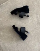 Sandalias de cuero vacuno color negro, con taco de cuña y tira ancha sobre el empeine. Ajuste con hebilla al tobillo.