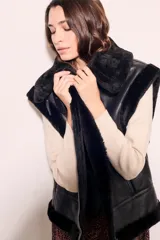 Chaleco negro de cuero sintético con cuello de piel sintética y cierre frontal con cremallera.