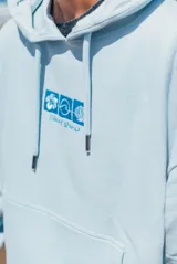 Hoodie celeste con capucha, de corte holgado, con bordado en la espalda que incluye flores de hibisco y texto decorativo en tonos azules.