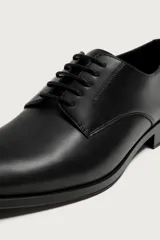 Zapato de vestir tipo derby en color negro, con diseño de parte superior lisa, horma redonda y suela con ligero tacón.