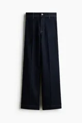Jean wide leg de tiro alto en denim azul oscuro con costuras en tono contraste, trabillas para cinto y cierre frontal con botón metálico.