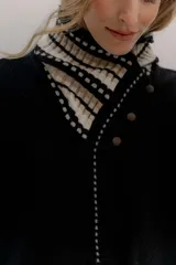 Polera tejida en lambswool color beige, con cuello alto y diseño de intarsia en tonos marrones y grises. Presenta botones forrados en el cuello para modular la apertura.