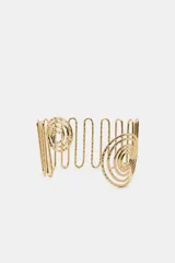 Brazalete rígido de metal dorado con diseño de estructura ondulada y extremos decorados con espirales circulares.