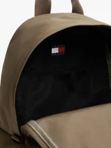 Mochila de diseño redondeado en color marrón, confeccionada en poliéster texturizado. Cuenta con un compartimento principal con cierre, un bolsillo exterior con cremallera y un bolsillo interior de malla. Incluye asa superior y correas ajustables y acolchadas. Presenta un parche tejido con el logo de Tommy Jeans en la parte delantera.