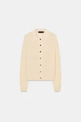 Chaqueta de punto color crema, manga larga, con cuello solapa y cierre frontal de botones oscuros.