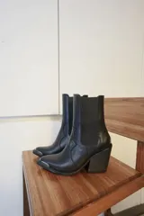 Botas texanas de cuero negro con paneles elásticos laterales, taco cuadrado y puntera metálica decorativa.