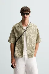 Camisa de manga corta y corte relajado confeccionada en tejido de algodón con diseño jacquard floral. Presenta cuello bowling, un bolsillo de plastrón en el pecho y cierre frontal con botones.