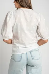 Blusa marrón de algodón con bordados sutiles, escote en V, mangas cortas abullonadas y detalle de fruncido con cordón ajustable en el centro del frente.