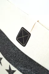 Bolso tipo tote color beige con estampado de estrellas negras, franja superior con brillos negros y asas de hombro en tono crudo.