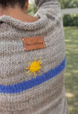 Sweater de punto en tonos beige con efecto degradado, cuello redondo y manga larga. Presenta una franja horizontal en color azul y el bordado de las letras 'SM' en color rojo en el pecho.