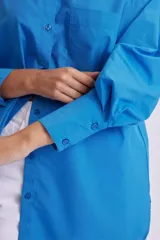 Camisa celeste de manga larga, corte oversize, con cuello clásico, cierre frontal con botones, bolsillo en el pecho y bajo redondeado.