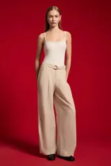 Pantalón ancho de lyocell color beige con pinzas en la parte delantera, tiro alto y un cinturón delgado con hebilla redonda metálica.