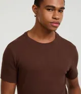 Remera muscle de hombre, color marrón claro, confeccionada en media malla, de cuello redondo y manga corta.