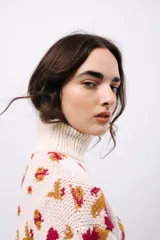Polera de tejido de punto con cuello alto, diseño holgado y estampado jacquard con motivos geométricos y figuras en tonos beige, naranja y celeste.