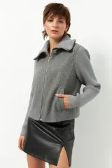 Tapado corto gris con cuerpo de paño y mangas tejidas. Presenta cuello alto, cierre frontal con cremallera y bolsillos laterales.