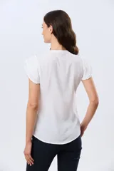 Blusa blanca sin mangas con volados en los hombros, cuello redondo con aberturas y cierre frontal parcial con botones.