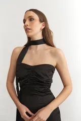 Vestido midi sin mangas color turquesa, con escote strapless y detalle de nudo frontal. El ruedo presenta un corte asimétrico con flecos negros largos.
