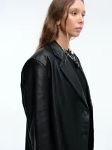 Blazer de ecocuero negro con silueta estructurada, solapas clásicas y cierre frontal mediante botones.