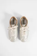 Zapatilla baja de microfibra color gris plateado, con diseño aerodinámico, costuras pespuntadas en contraste blanco, cordones blancos y suela de goma marrón con textura de tapones.