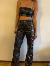 Pantalón de cuero sintético negro, de tiro alto y corte acampanado, con aberturas geométricas en las piernas.