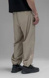 Pantalón deportivo de microfibra color beige, con corte regular y diseño de inspiración vintage. Presenta vivos laterales a contratono, cintura elástica y puños elásticos en los tobillos.