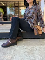 Botas cortas de cuero color marrón con suela track negra. Presentan dos correas ajustables con hebillas metálicas plateadas en el empeine y cierre lateral interno.