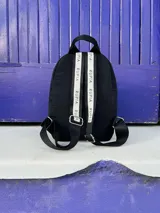 Mochila negra de nylon con cierre plateado y etiqueta con el logo de la marca en color beige.