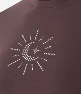 Remera baby tee de algodón color marrón oscuro, con cuello redondo, manga corta y calce ajustado. Presenta un aplique frontal de pedrería brillante con diseño místico de sol, luna y estrella.