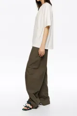 Pantalón de algodón color beige, de corte barrel ancho con tiro bajo. Presenta bolsillos en costuras delanteros y con vivo en la parte trasera. El bajo de la pierna tiene trabillas para ajustar el volumen.