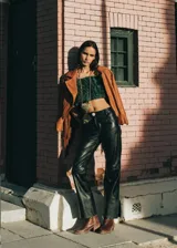 Pantalón de cuero color marrón con estampado abstracto, corte acampanado y abertura en el ruedo.