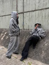 Campera con capucha gris oscura, cierre frontal y diseño oversize con doble capucha, incluyendo balaclava integrada. Presenta gran estampa contrastante en el frente.