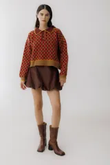 Buzo de tejido de punto con diseño de rombos en tonos beige y marrón. Presenta cuello polo con cierre frontal de tres botones, mangas largas con puños acanalados y ruedo también acanalado.