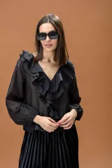 Camisa negra de manga larga con volados frontales y cuello en V. Presenta puños elásticos y una caída fluida.