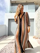 Vestido largo de tejido de punto con diseño geométrico en tonos tierra, negro y blanco. Presenta escote en V profundo, mangas tres cuartos y tajos laterales en la falda.