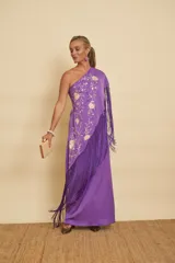 Vestido largo morado de un solo hombro, con detalles bordados florales en tono crudo y un gran mantón con flecos largos del mismo color.