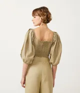 Blusa cropped de tricolina color beige, con escote corazón, detalle cruzado delantero y mangas 3/4 abullonadas. Posee lastex en la espalda para ajuste.